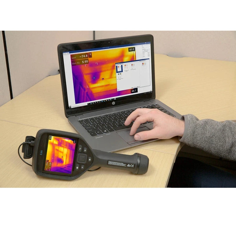 Person using a FLIRE86 thermal imaging device connected to a laptop on a table.